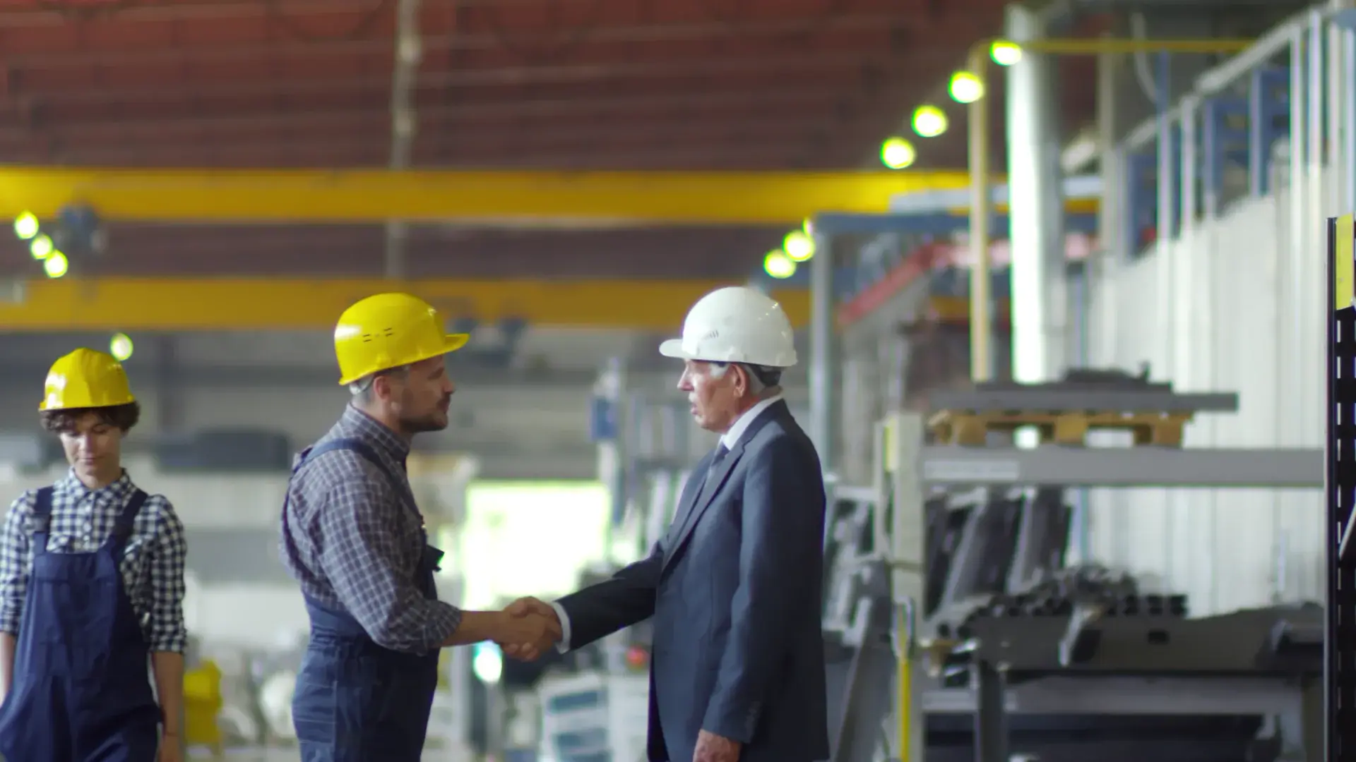 Two professionals in hard hats shaking hands on a factory floor